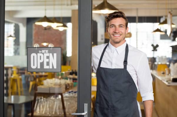 Man stands at the entrance to his business with an open sign
